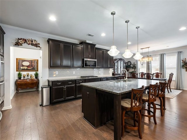 kitchen featuring sink, light stone counters, a center island with sink, appliances with stainless steel finishes, and pendant lighting