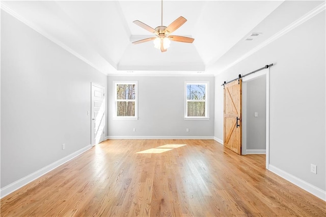 spare room featuring ceiling fan, a tray ceiling, a barn door, and light wood-type flooring