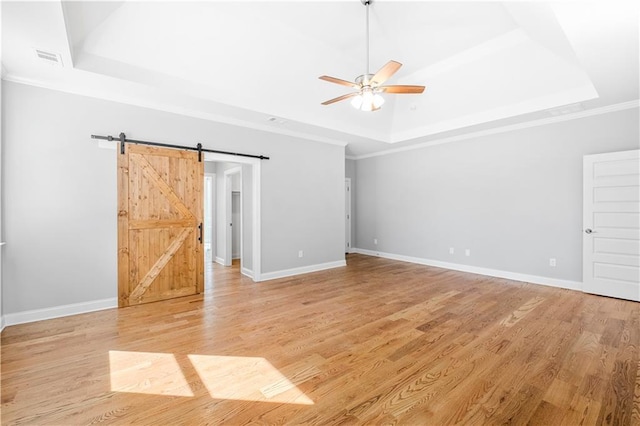 spare room featuring a raised ceiling, a barn door, ceiling fan, and light hardwood / wood-style flooring