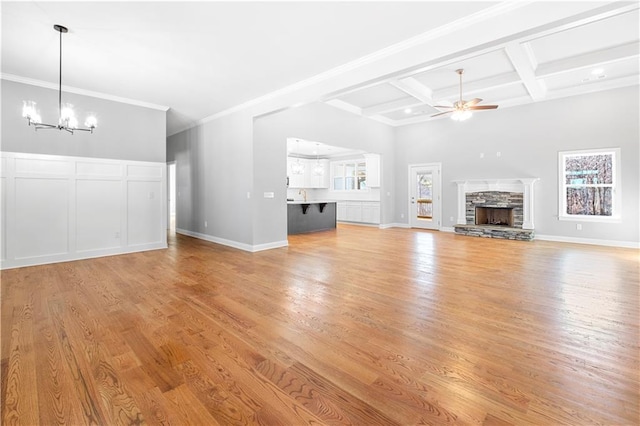 unfurnished living room featuring ceiling fan with notable chandelier, a stone fireplace, beamed ceiling, light wood-type flooring, and coffered ceiling