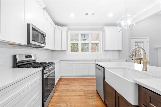 kitchen with white cabinets, appliances with stainless steel finishes, decorative light fixtures, a chandelier, and light hardwood / wood-style flooring