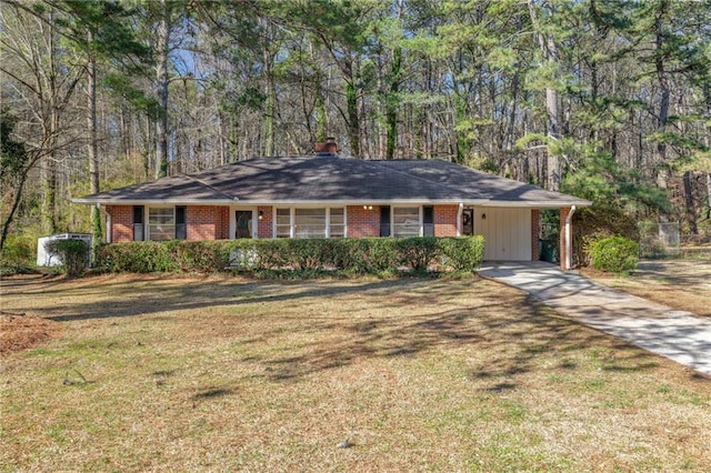 single story home featuring driveway, a front lawn, a forest view, and brick siding