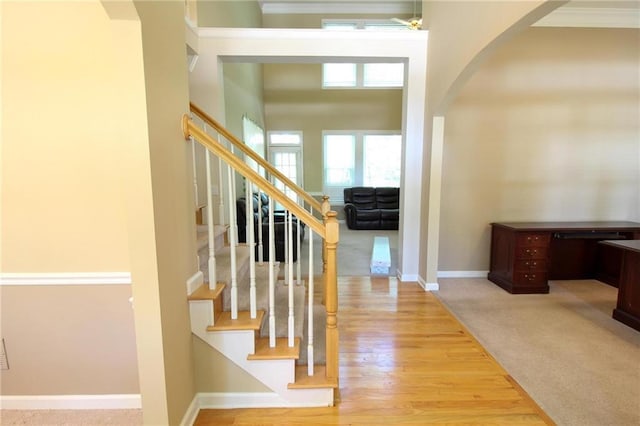 foyer with baseboards, crown molding, wood finished floors, arched walkways, and stairway