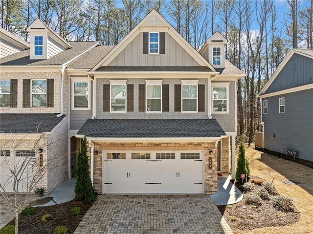 view of front facade with an attached garage, decorative driveway, stone siding, board and batten siding, and roof with shingles