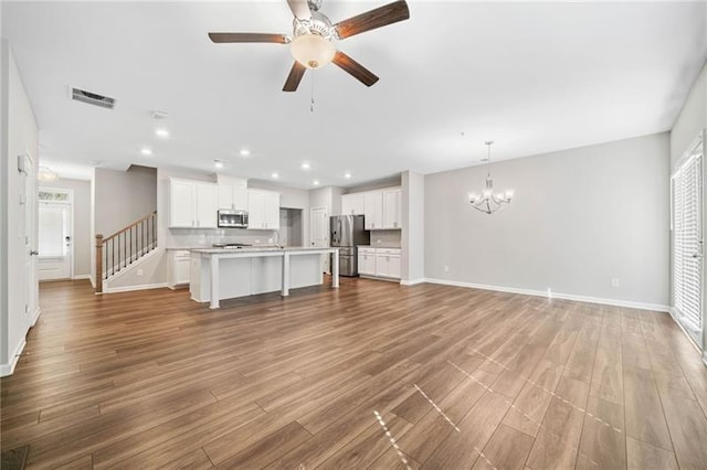 unfurnished living room featuring ceiling fan, a chandelier, wood finished floors, baseboards, and recessed lighting