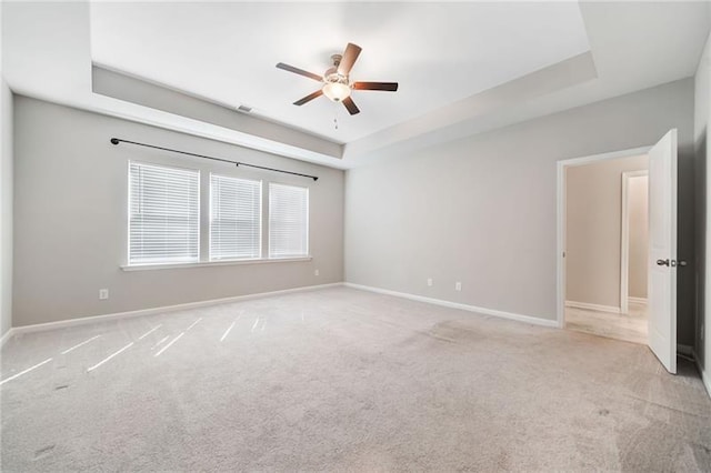 unfurnished room with a raised ceiling, a ceiling fan, light colored carpet, and baseboards