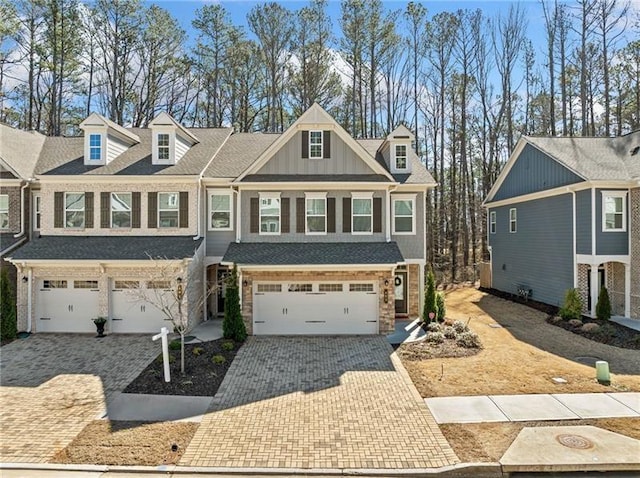 view of front facade featuring an attached garage, stone siding, decorative driveway, and board and batten siding