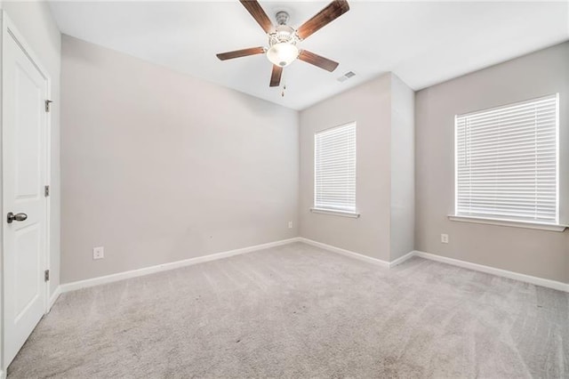 empty room featuring light colored carpet, a ceiling fan, and baseboards