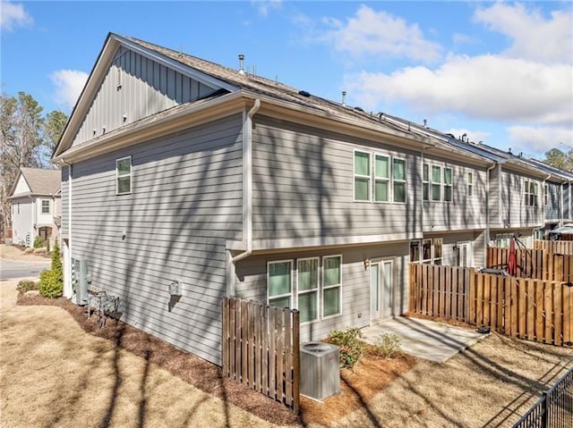 rear view of house featuring board and batten siding, a patio, cooling unit, fence, and a residential view