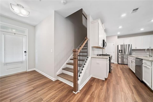 kitchen featuring appliances with stainless steel finishes, a sink, wood finished floors, white cabinets, and light stone counters