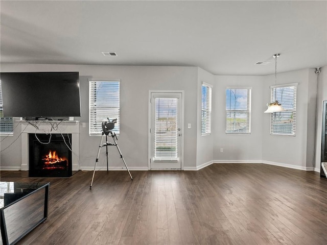 unfurnished living room featuring a healthy amount of sunlight, dark wood-type flooring, visible vents, and a fireplace