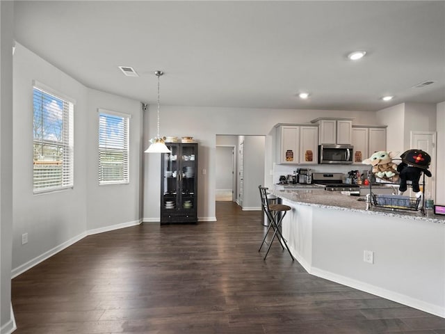 kitchen with dark wood-style floors, light stone counters, stainless steel appliances, decorative light fixtures, and baseboards
