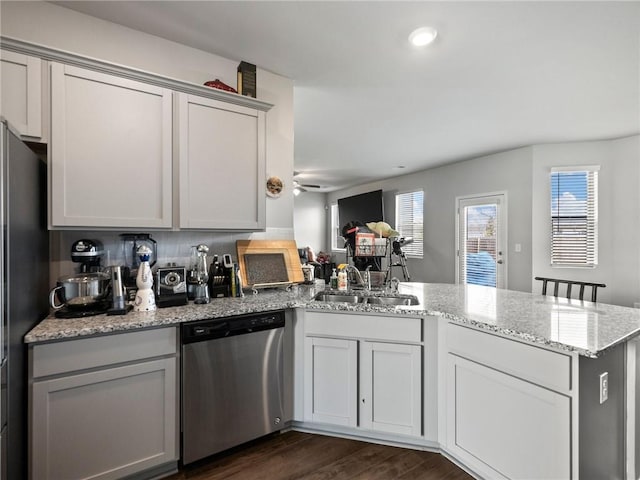 kitchen with dark wood-style floors, dishwasher, a sink, freestanding refrigerator, and a peninsula