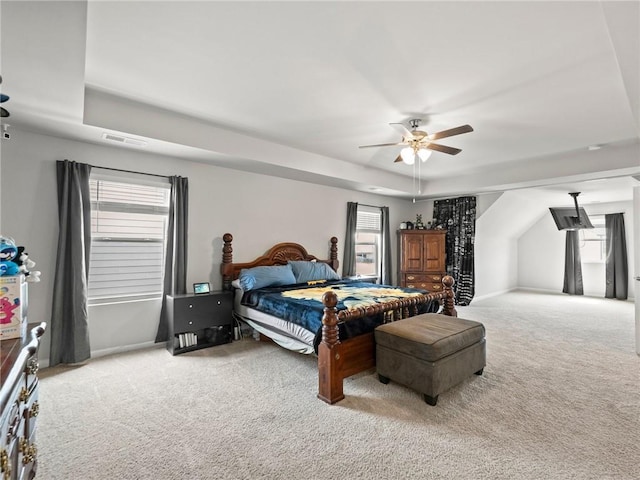carpeted bedroom featuring a ceiling fan, visible vents, a raised ceiling, and multiple windows