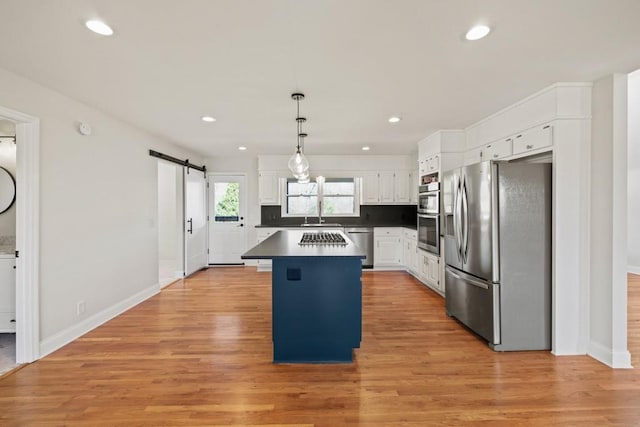 kitchen with dark countertops, a kitchen island, a barn door, white cabinets, and stainless steel appliances