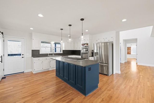 kitchen featuring dark countertops, a sink, stainless steel appliances, white cabinets, and a barn door