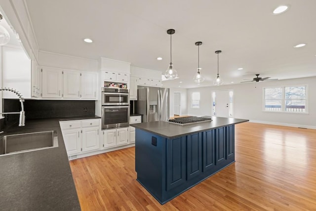 kitchen with a sink, dark countertops, stainless steel appliances, white cabinets, and light wood finished floors