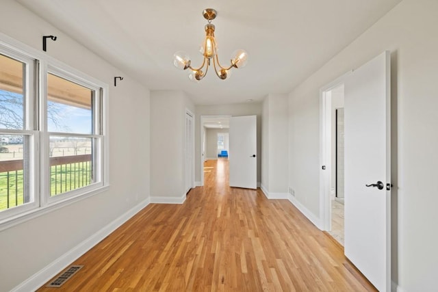 hallway featuring a notable chandelier, baseboards, visible vents, and light wood finished floors