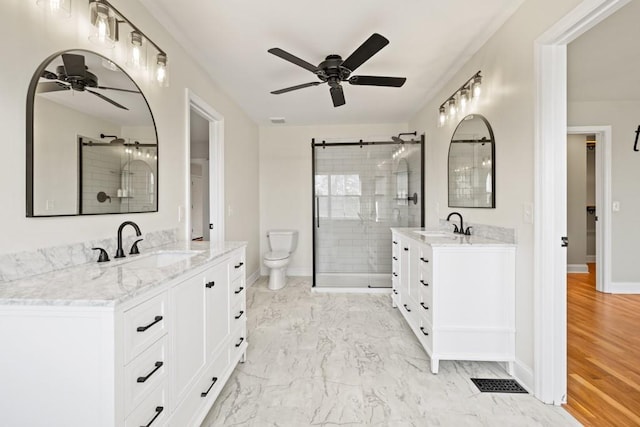 full bathroom featuring two vanities, a stall shower, a ceiling fan, a sink, and baseboards