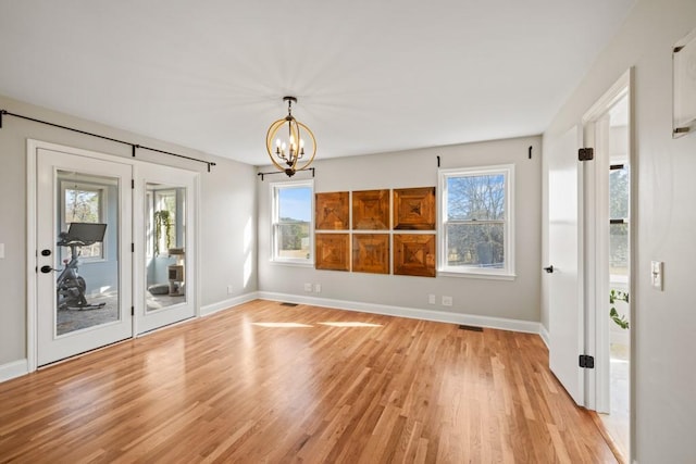 spare room featuring a chandelier, visible vents, light wood-type flooring, and baseboards