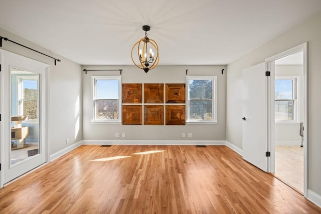 empty room with baseboards, plenty of natural light, a chandelier, and light wood finished floors