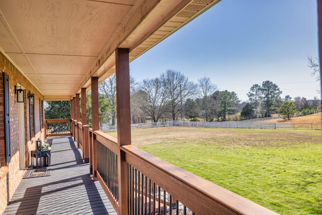 deck with a rural view, a lawn, a porch, and fence