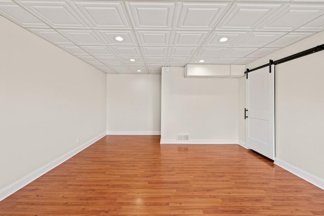 finished basement with recessed lighting, baseboards, light wood-style floors, and a barn door