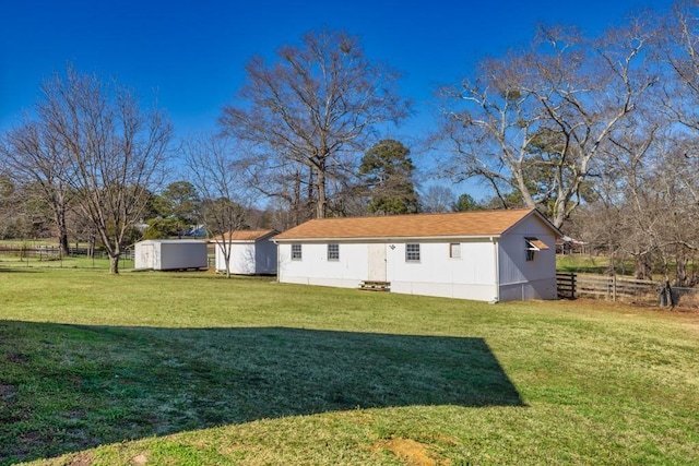 rear view of house with a yard, a storage shed, an outdoor structure, and fence