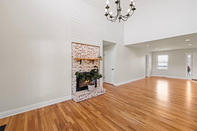 unfurnished living room with visible vents, a large fireplace, baseboards, an inviting chandelier, and wood finished floors