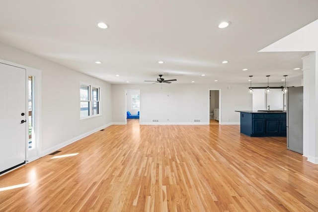 unfurnished living room with a sink, light wood-type flooring, baseboards, and recessed lighting