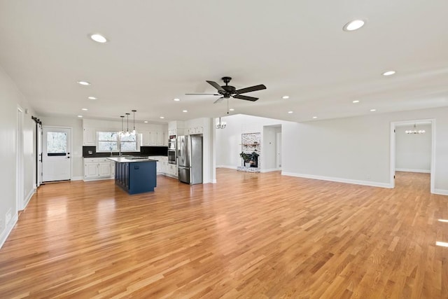 unfurnished living room with recessed lighting, light wood finished floors, a fireplace with raised hearth, and ceiling fan with notable chandelier