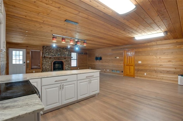 kitchen with wooden walls, wooden ceiling, white cabinetry, hanging light fixtures, and a stone fireplace