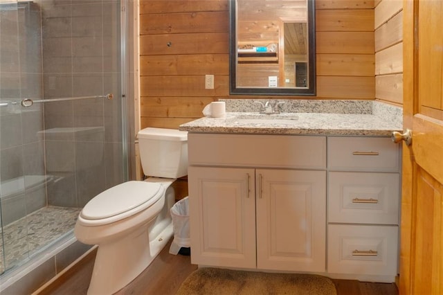 bathroom with vanity, a shower with door, wood-type flooring, toilet, and wood walls