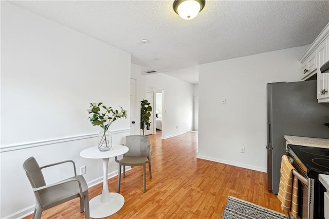 kitchen featuring a textured ceiling, white cabinets, light hardwood / wood-style floors, and stainless steel electric range