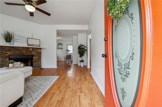 foyer featuring a stone fireplace, light hardwood / wood-style floors, and ceiling fan