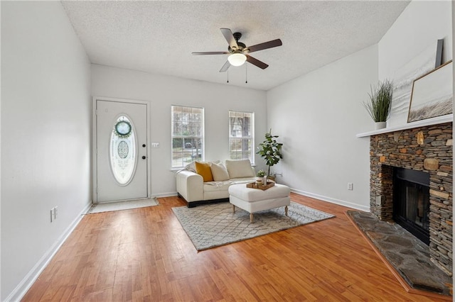 unfurnished living room with ceiling fan, a stone fireplace, a textured ceiling, and light wood-type flooring