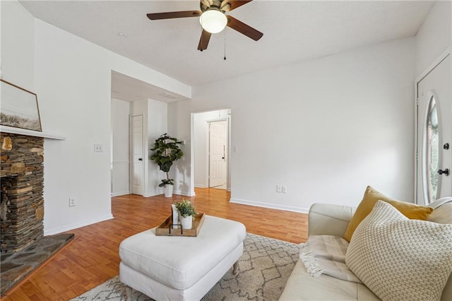 living room featuring a stone fireplace, ceiling fan, and light wood-type flooring