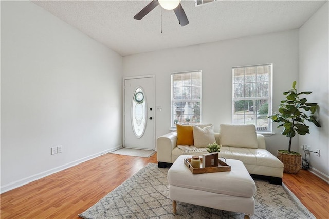 living room with ceiling fan, a textured ceiling, and light hardwood / wood-style floors