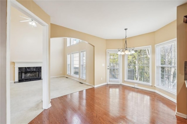 unfurnished dining area featuring carpet, a healthy amount of sunlight, ceiling fan with notable chandelier, and a high end fireplace