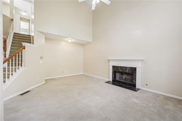 unfurnished living room with light carpet, a towering ceiling, a fireplace, and ceiling fan