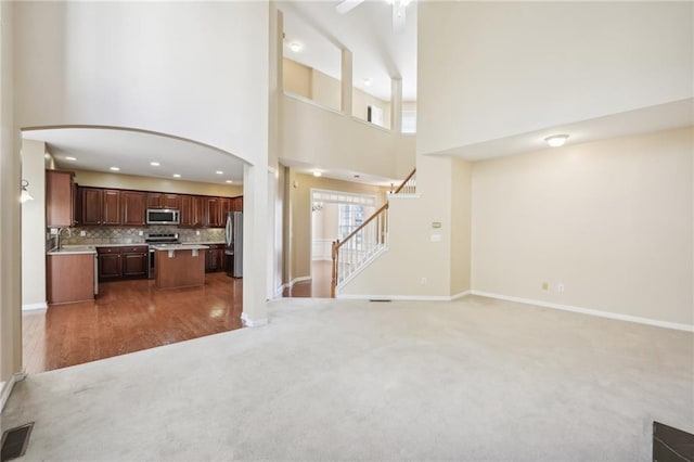 unfurnished living room with a towering ceiling, sink, ceiling fan, and carpet flooring