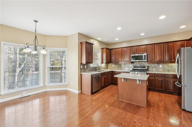 kitchen with hardwood / wood-style flooring, appliances with stainless steel finishes, decorative light fixtures, and a kitchen island