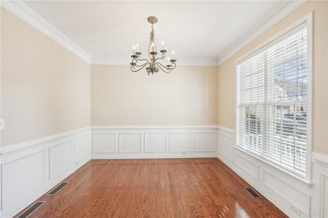 spare room with an inviting chandelier, crown molding, a healthy amount of sunlight, and light wood-type flooring