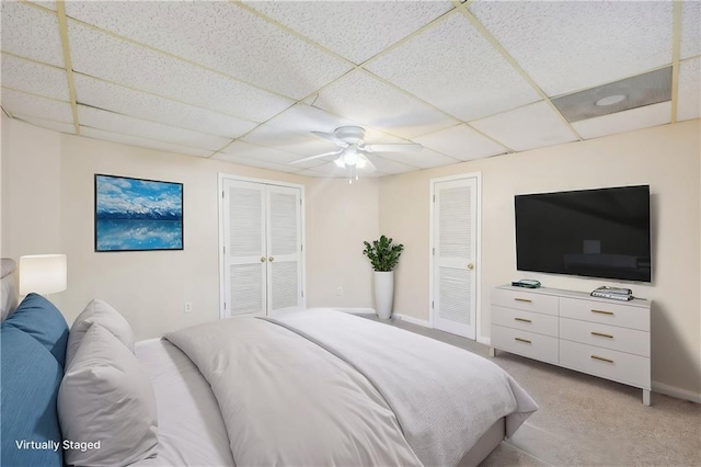 bedroom with two closets, light carpet, a drop ceiling, and ceiling fan