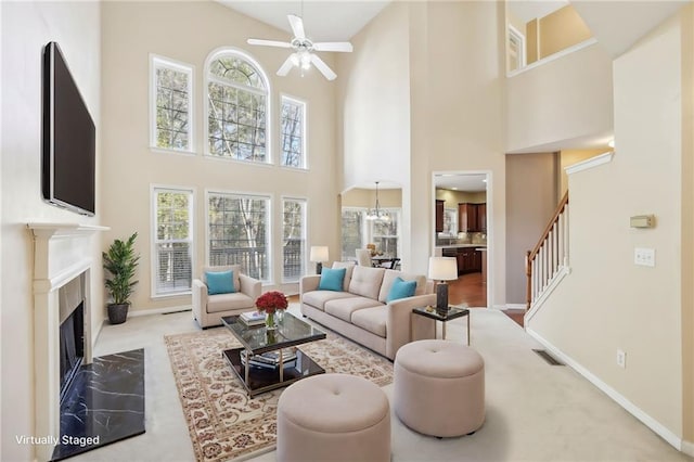 carpeted living room with a towering ceiling, a fireplace, and ceiling fan with notable chandelier