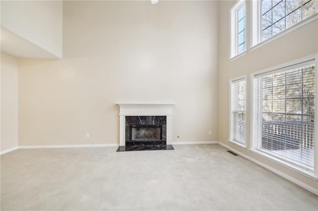 unfurnished living room with a high end fireplace, carpet, and a high ceiling