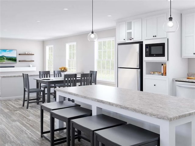 kitchen with pendant lighting, white cabinetry, fridge, and black microwave