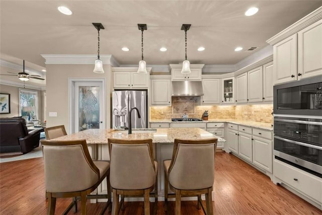 kitchen with light stone counters, a kitchen island with sink, hanging light fixtures, and black appliances