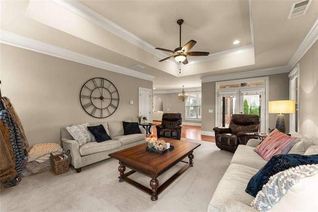 living room with crown molding, a tray ceiling, ceiling fan with notable chandelier, and light hardwood / wood-style floors