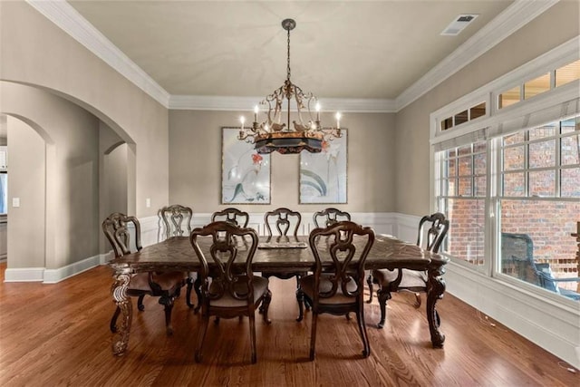 dining space with hardwood / wood-style flooring, ornamental molding, and a notable chandelier